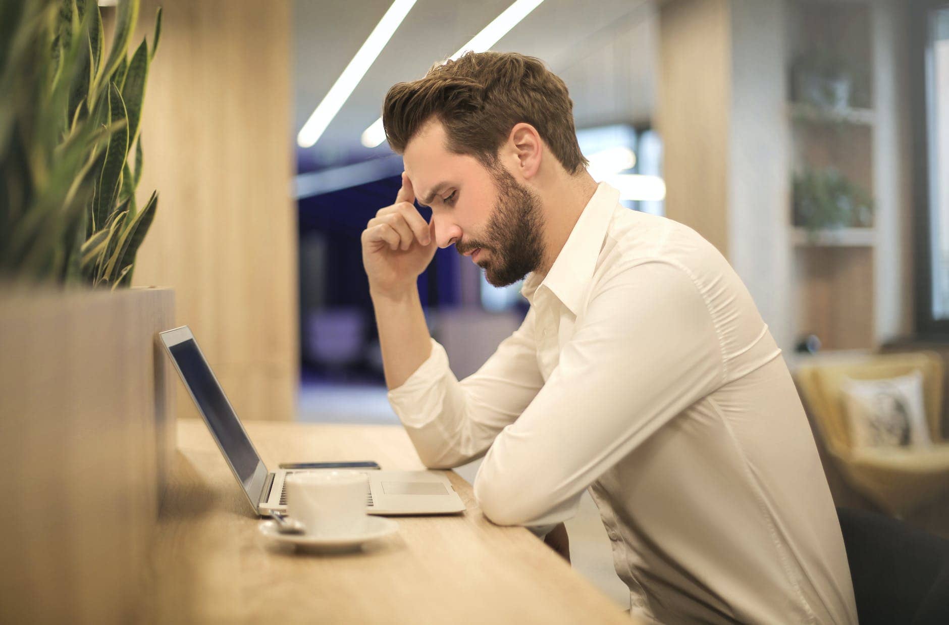 man with hand on temple looking at laptop - business crisis