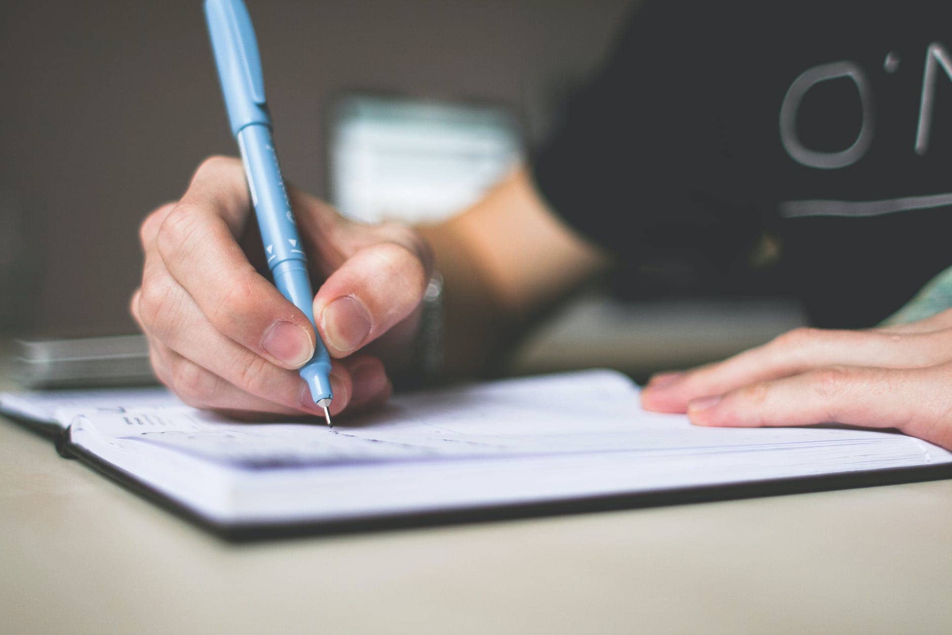 person holding blue ballpoint pen writing in notebook - how to become a better writer