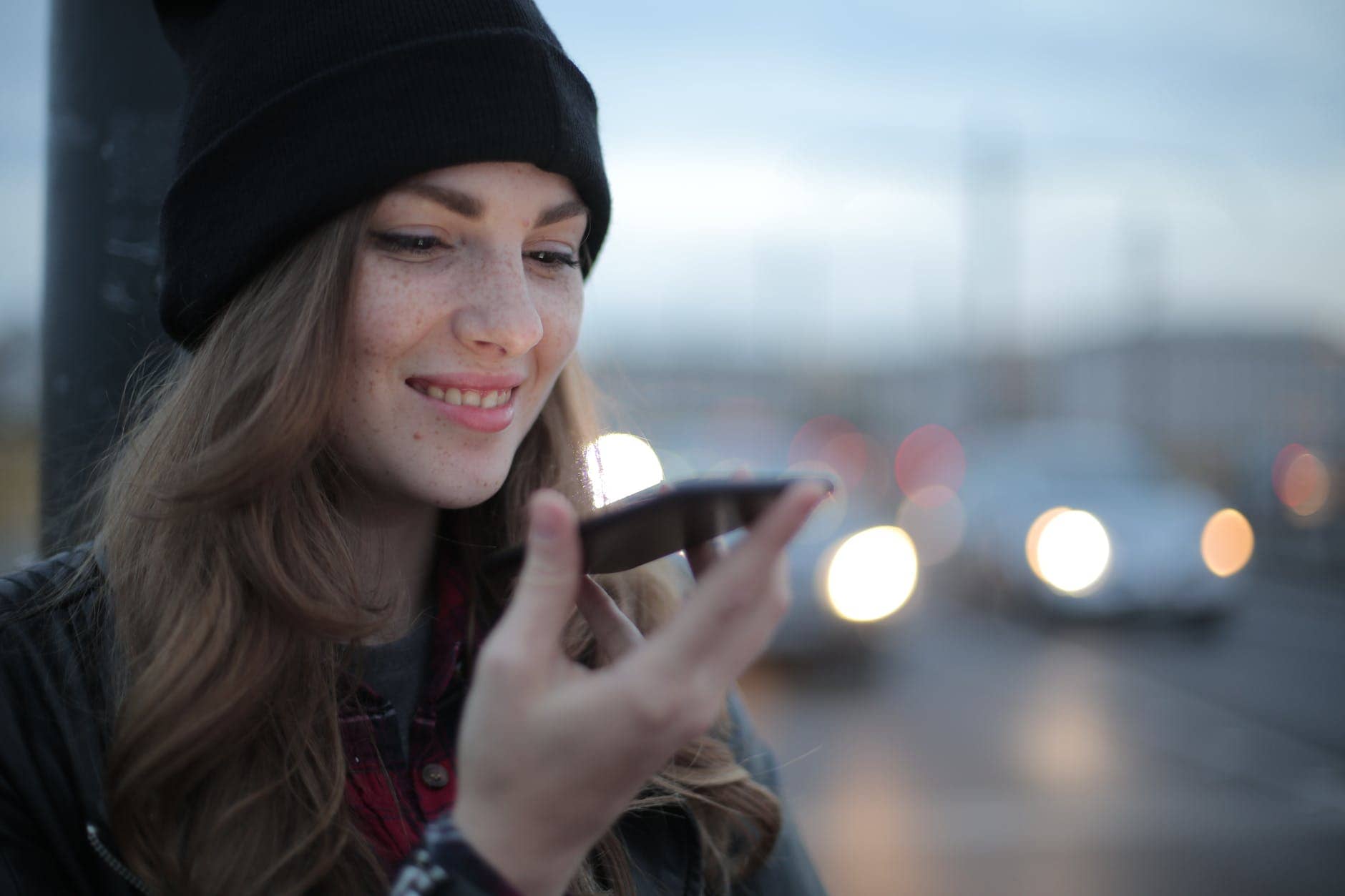 joyful young woman phoning on street in evening - voice search optimization