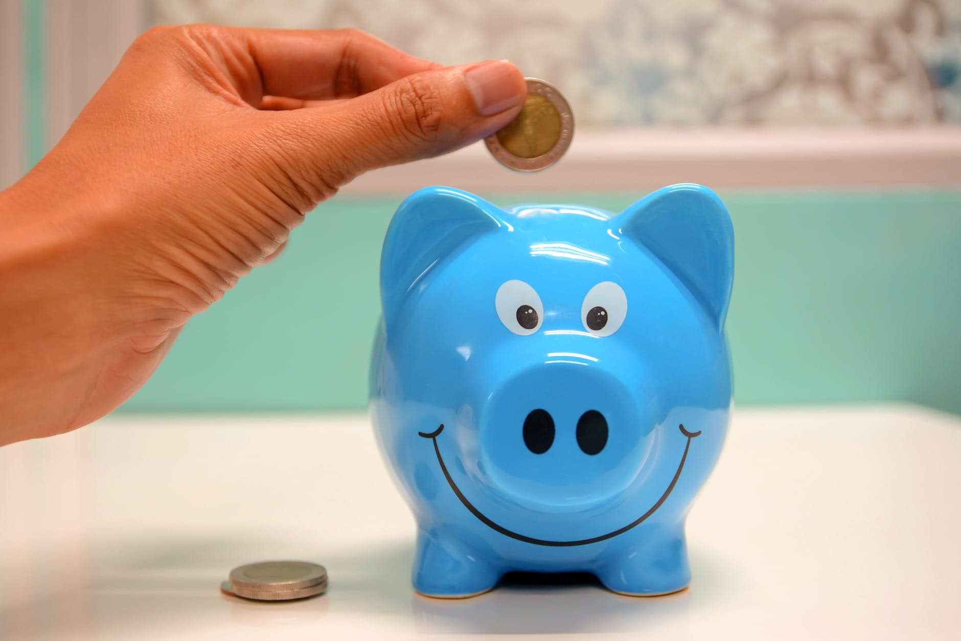 person putting coin in a piggy bank - How to Get Out of Debt on a Low Income